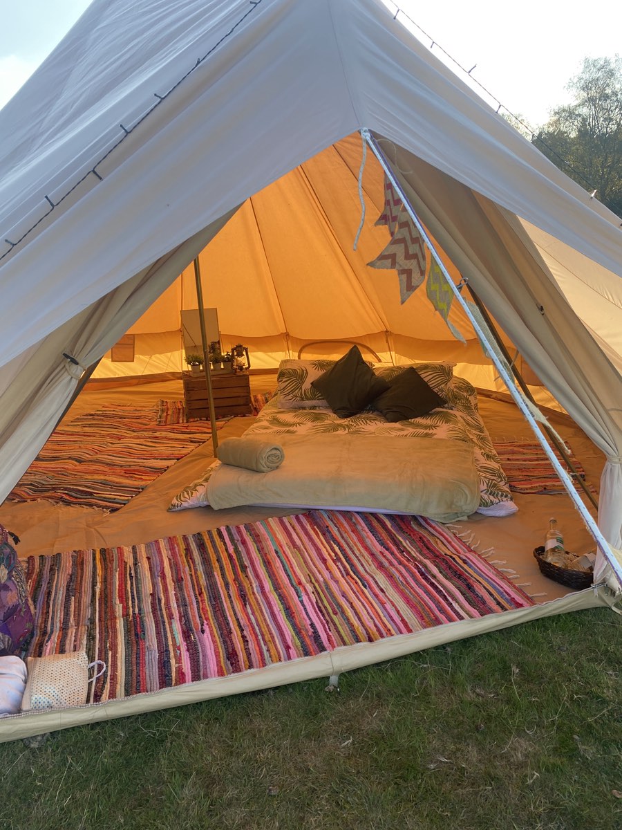 Inside a bell tent: a made-up bed, cushions and bright rag rugs