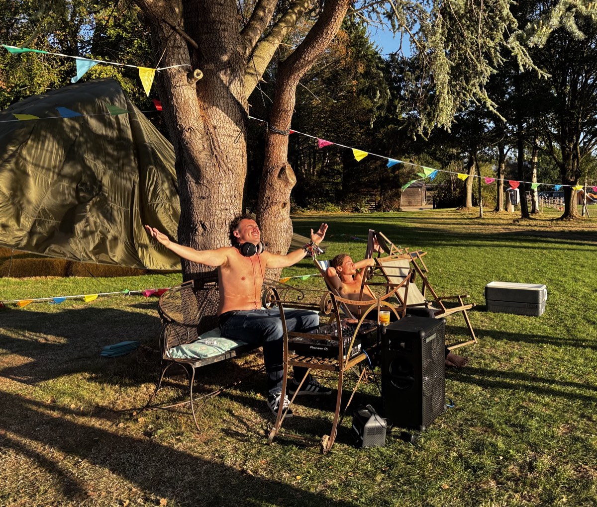 A DJ with his arms wide under the big tree, bunting overhead