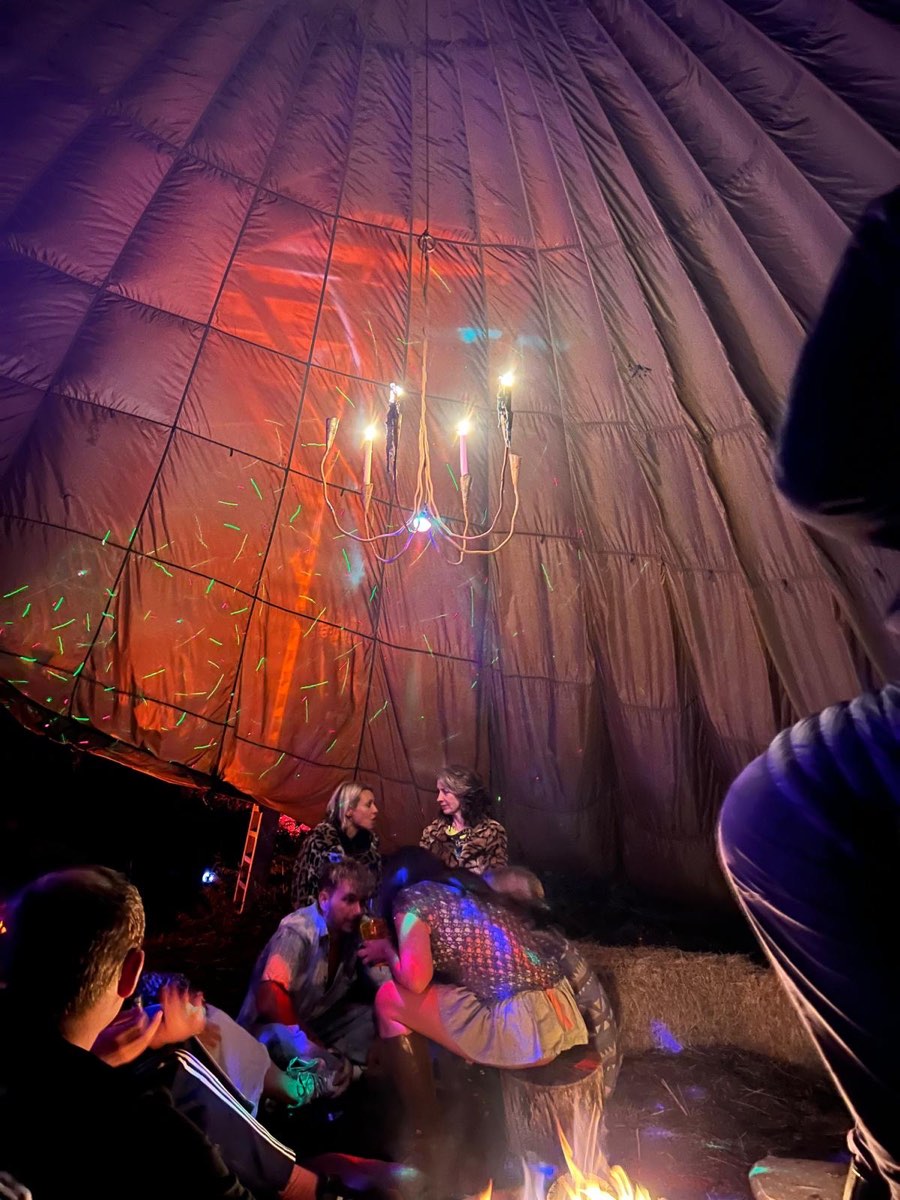 Friends round a fire inside the tipi, under a candle chandelier