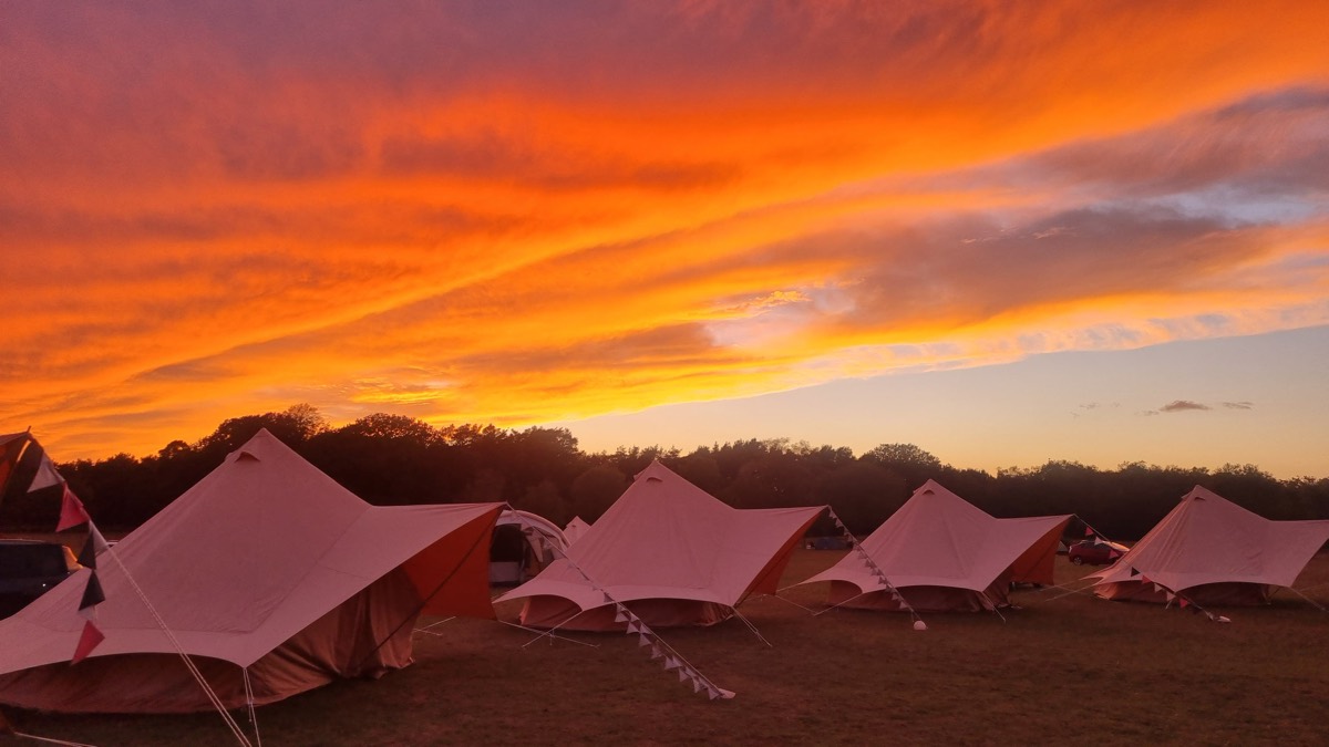 A row of bell tents with bunting under a blazing orange sunset