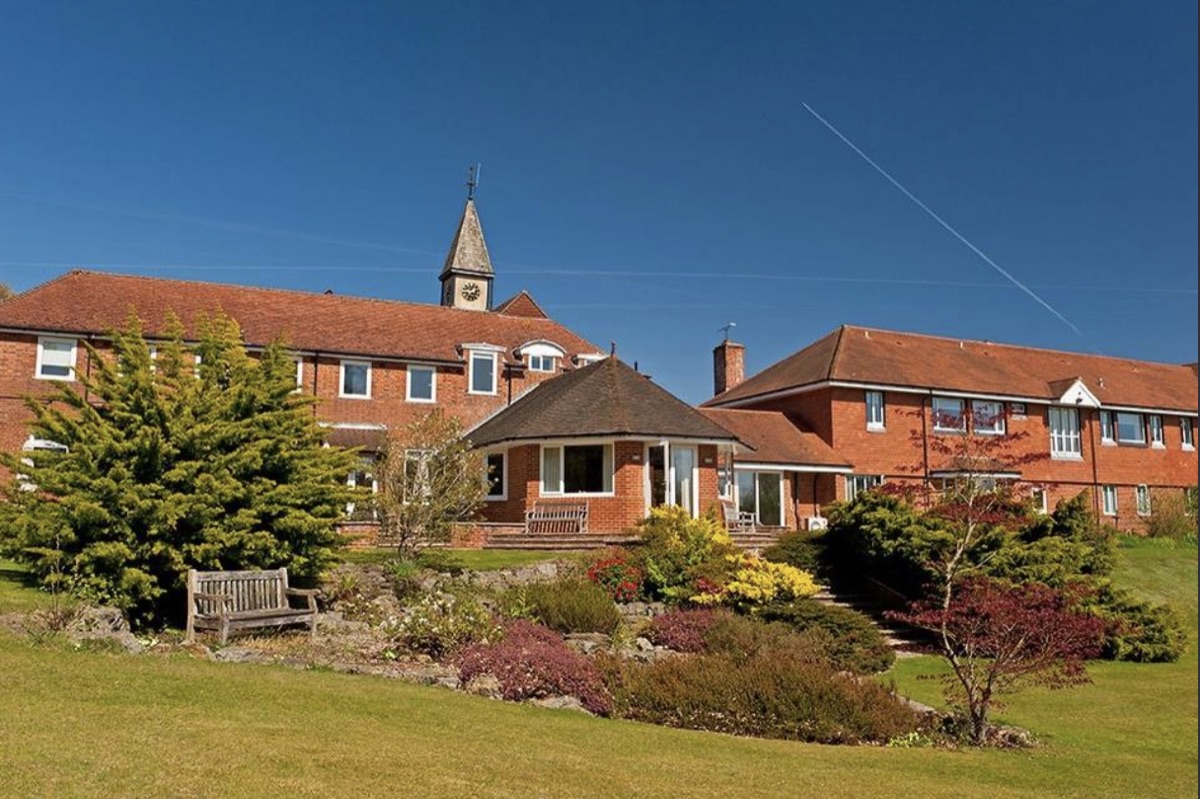 A red-brick country house with a clock tower, lawns and flower beds under a blue sky