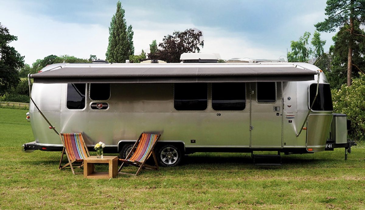 A silver Airstream trailer on the grass with two deckchairs and a little table